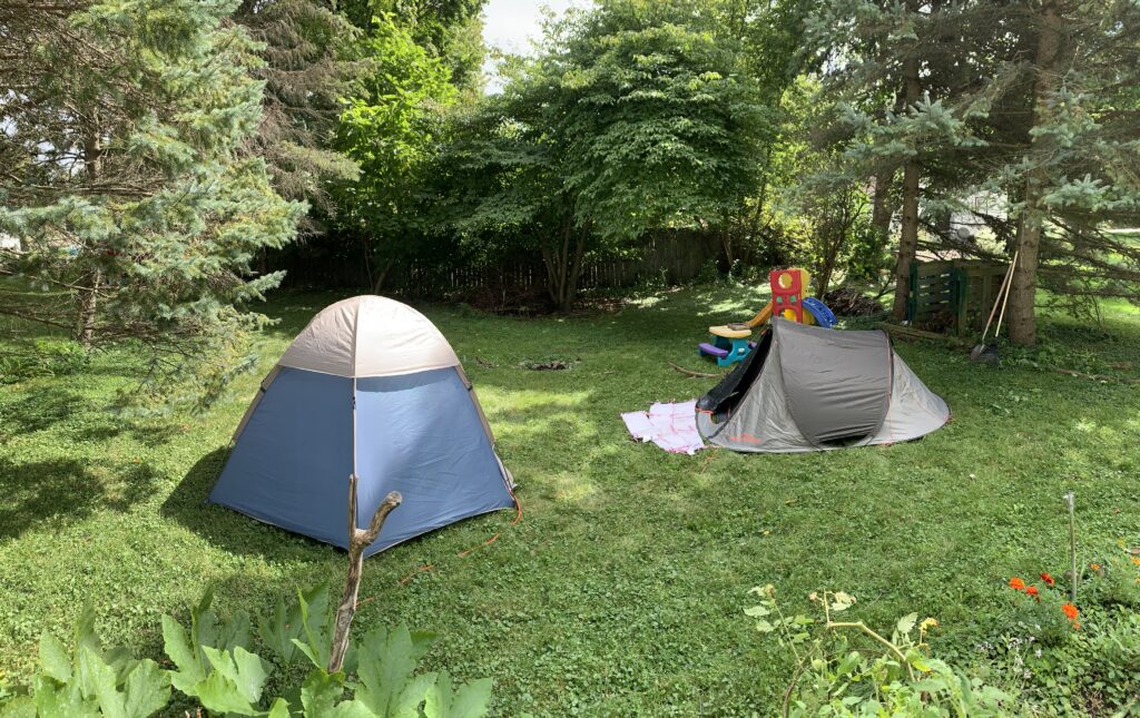 Wide shot of our backyard campsite: two tents, campfire, and a toddler picnic table.