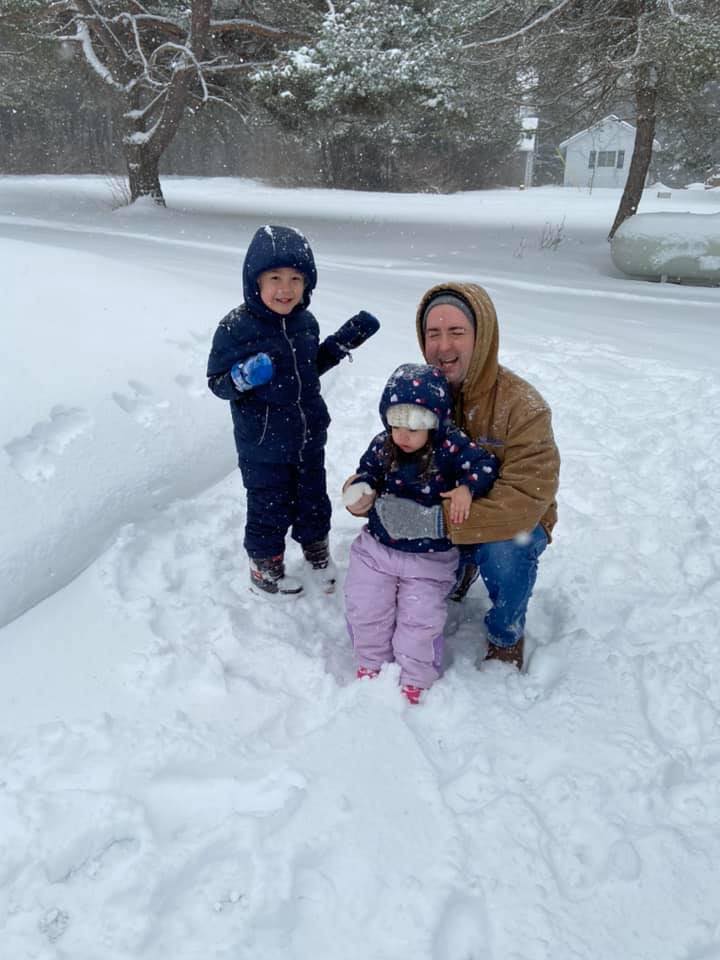Two kids and their dad pose for a photo while playing in the snow. Snowfall; snowpants; Carhartt jacket