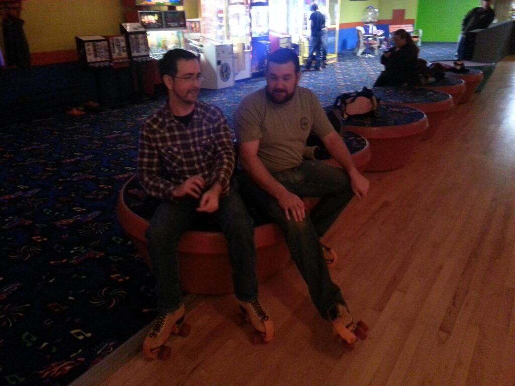 two men putting on their skates at the edge of a roller rink.