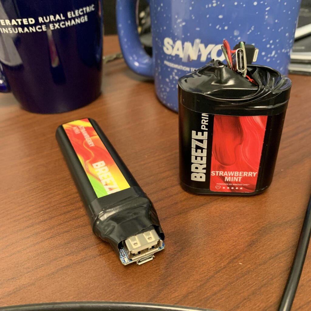 Two disposable vape, wrapped with electrical tape, with pieces of electronic components sticking out.